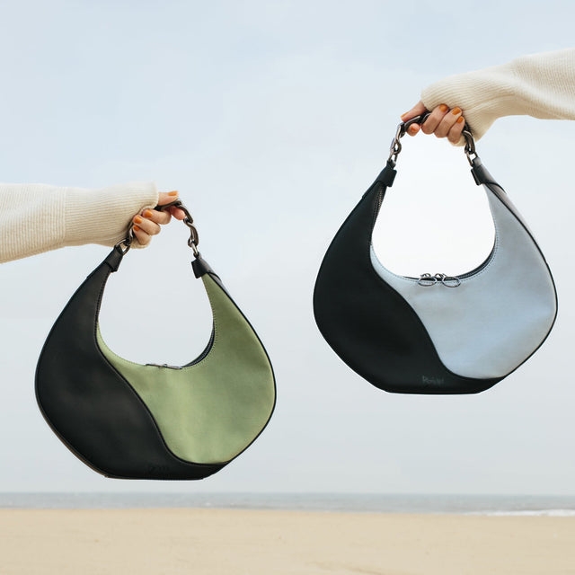 Both color options for the Mariah Bag shown on the beach. Blue or green organic cotton and black cactus leather