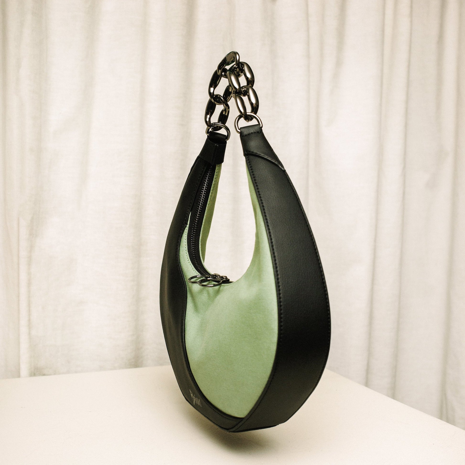 Side shot of Mariah handbag by Brinn, crafted with black cactus leather, green organic cotton, and a smooth gunmetal chain as the handle